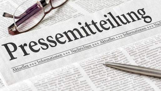 Zeitung mit der Überschrift Pressemitteilung mit Brille und Kuli