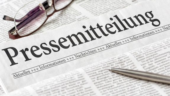 Zeitung mit der Überschrift Pressemitteilung Zeitung mit der Überschrift Pressemitteilung mit Brille und Kuli