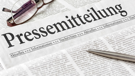 Zeitung mit der Überschrift Pressemitteilung mit Brille und Kuli