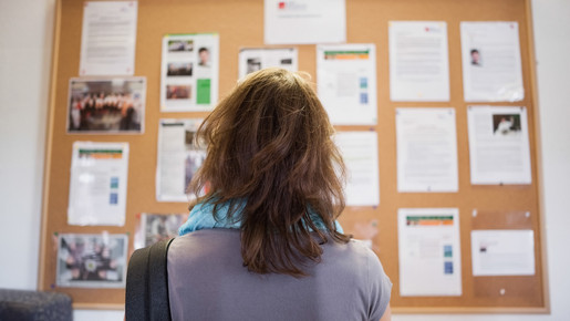 Frau steht vor einer Wandzeitung und liest Aushänge